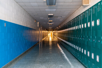 Green metal lockers along a nondescript hallway in a typical US High School.  No identifiable information included and nobody in the hall.  	