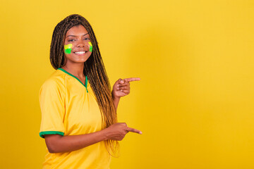 black woman young brazilian soccer fan. pointing finger to the right, smiling, publicity photo.