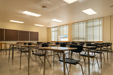 Example of an empty nondescript US High School Classroom with desks, window and black board.