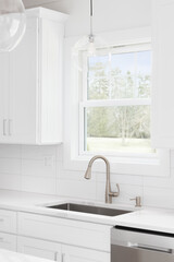 A kitchen sink detail with white cabinets, pendant lights hanging from the ceiling, and a tiled backsplash.
