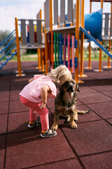 Little girl clung her head to a sitting dog on the playground. High quality photo