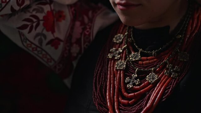Ukrainian woman takes off authentic jewelry necklace. She is in national costume of Ukraine - vyshyvanka and ancient coral beads, Zgarda - archaic hutsul neck ornament of status religious purpose