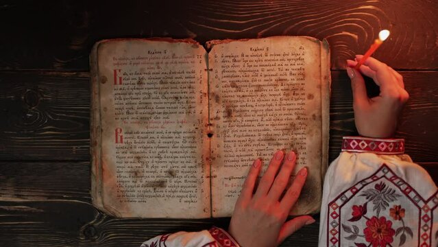 Ukrainian woman reading ancient book - Bible. Concentrated attentively follows finger on paper page under candle light. History of Kyiv Rus. Psalter, 19th century, prayers and psalms