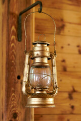 close up, a golden kerosene lamp hangs on a hook black on a pine wood wall, wall in a bright room, the lamp shows paint abrasions, dirty glass
