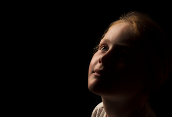 Young Caucasian girl looking upwards just away from the light with a very slight smile.