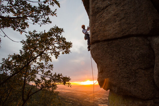 Skilled climber hanging on mountain while holding hand above green valley