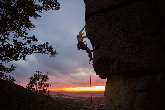 Skilled climber hanging on mountain while holding hand above green valley