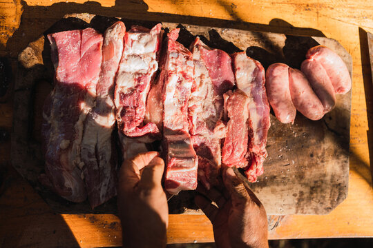 Anonymous cook preparing raw meat pieces and sausages on cutting board