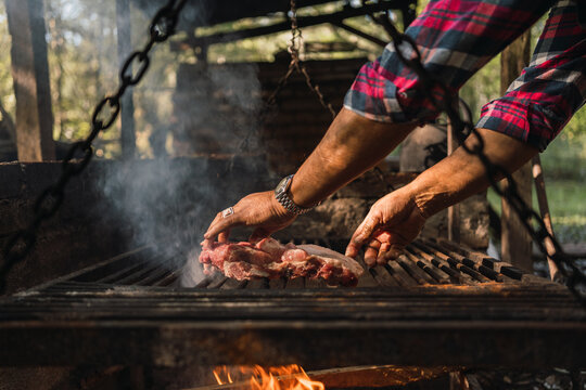 Anonymous man preparing raw meat pieces above burning fire