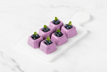 Blueberry cream cake, pudding in the form of small square portions, on a serving board. Light background	