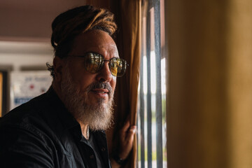 Confident man with dreadlocks looking at camera near window in house