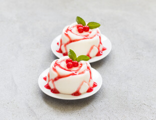 Vanilla cream dessert, Panna Cotta in the shape of a rose, with red currant sauce, on a plate. Light grey background