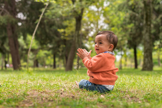 Cute Ethnic Boy Clapping Hands On Lawn