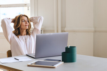 Contemplative businesswoman with hands behind head at creative office