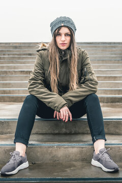 Beautiful young woman in fashionable casual clothes sits on step