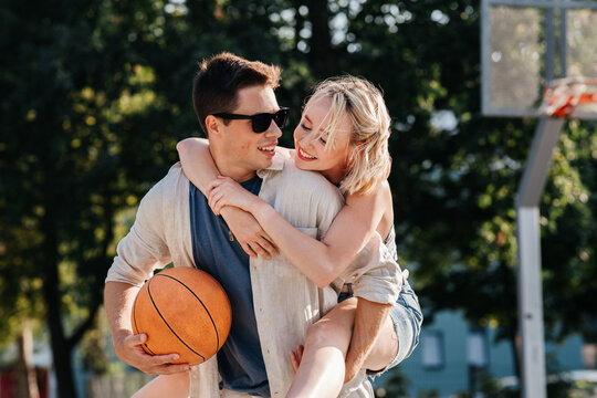 Summer Holidays, Love And People Concept - Happy Young Couple With Ball Having Fun On Basketball Playground