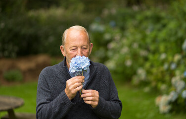 Old Caucasian male smelling a flower outdoors.