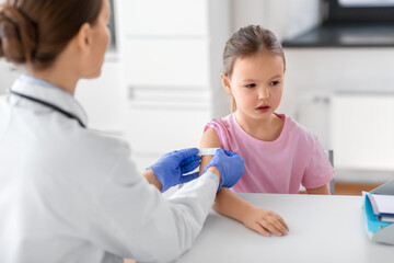 medicine, healthcare and vaccination concept - female doctor or pediatrician talking to little girl patient on medical exam at clinic