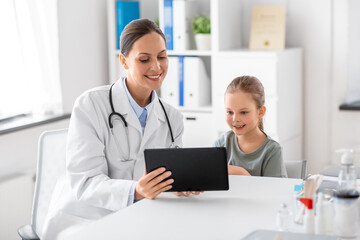 medicine, healthcare and pediatry concept - happy smiling female doctor or pediatrician showing tablet computer to little girl patient at clinic