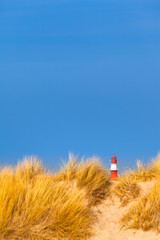 Coast Travel Landmark / Far red and white lighthouse at dune horizon under blue sky (copy space) - 527936300