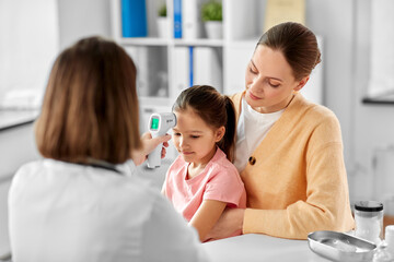 medicine, healthcare and pediatry concept - mother with sick little daughter and doctor measuring temperature with infrared forehead thermometer at clinic