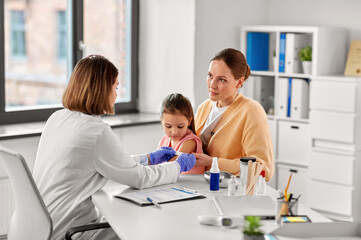 medicine, healthcare and pediatry concept - female doctor or pediatrician attaching medicinal patch to arm of little girl patient with mother at clinic