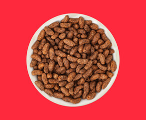 White bowl with natural organic granola cereal chocolate flakes on red background. Oven-toasted rice cereal and the flavor chocolate. Top view
