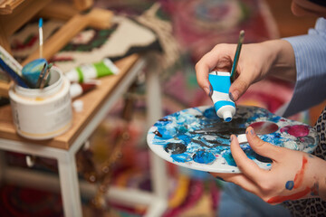 Close-up photo of a woman painting on canvas with a brush and tempera