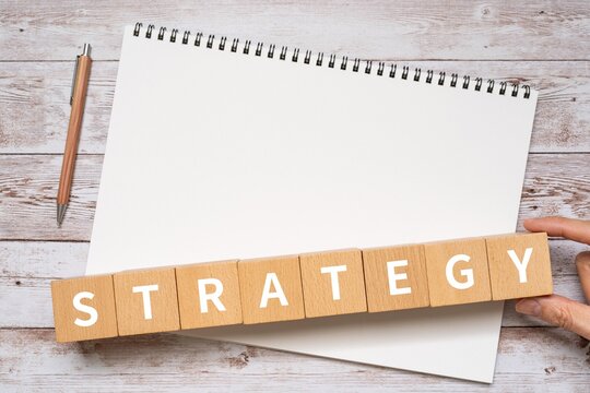 戦略・ストラテジーのイメージ｜STRATEGYと書かれたブロック、ノート、ペン、手
