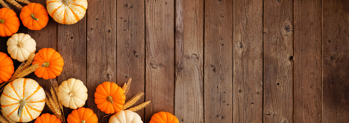 Fall corner border of orange and white pumpkins and wheat. Top down view on a rustic dark wood...