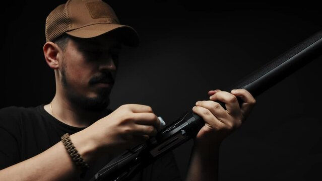 Close-up: a man in a black T-shirt on a black background loads a shotgun
