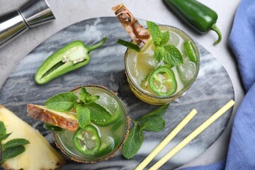 Glasses of spicy pineapple cocktail with jalapeno and mint on grey table, flat lay
