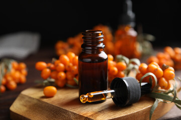 Ripe sea buckthorn and essential oil on wooden board against black background
