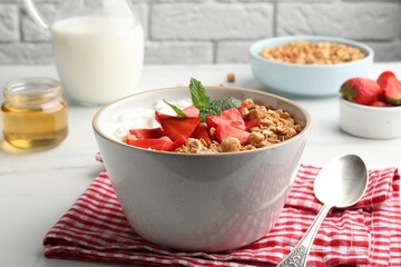 Bowl with tasty granola and strawberries served on white table. Healthy meal