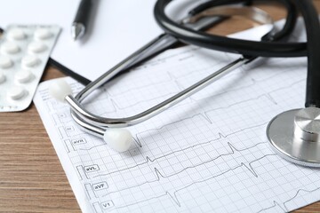 Cardiogram report, stethoscope and pills on wooden table, closeup