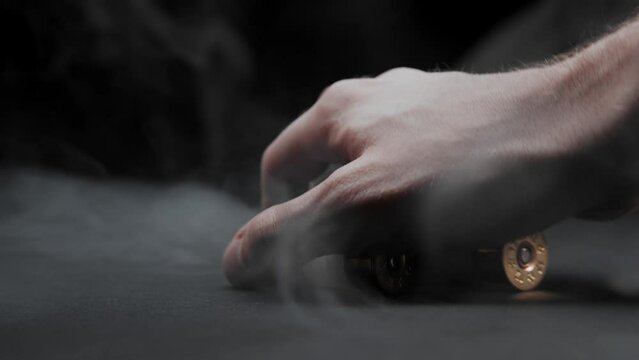 Close-up of a man picking up shotgun shells from a table against a dark background