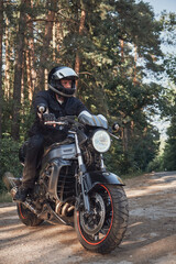 Fototapeta na wymiar Young male biker in a helmet travels on a motorcycle alone, on a road in the forest