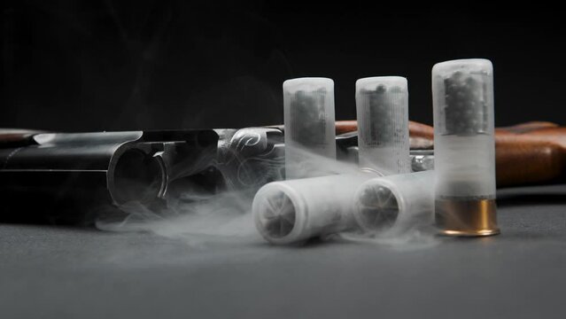 Close-up of a loaded shotgun after being fired and cartridges on a table in smoke