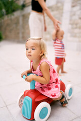 Little girl sitting on a toy car leaning forward. High quality photo