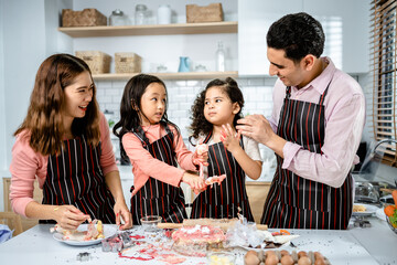 Happy multiethnic family cooking creams cake together in the kitchen at home. a parent teaches daughters to make homemade desserts, enjoy leisure activities time, family