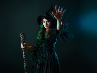 A witch with a staff sends a spell. Young witch in black dress and pointed hat, Halloween image