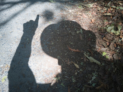 Sombra de un hombre con sombrero apuntando con su mano y dedo, sobre un camino.