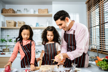 Happy multiethnic family cooking creams cake together in the kitchen at home. a father teaches daughters to make homemade desserts, enjoy leisure activities time