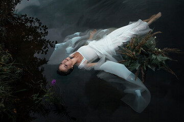 A river nymph swims in a backwater. A beautiful young woman in a mysterious image floats on the surface of the water, a woman in a white dress