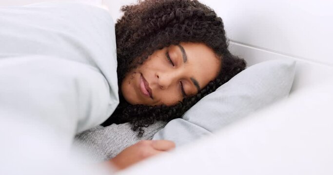 Young black woman sleeping in bed in her bedroom while resting and having a dream at home. Relax, peaceful and calm African girl taking a nap with a comfortable pillow and blanket at her house.