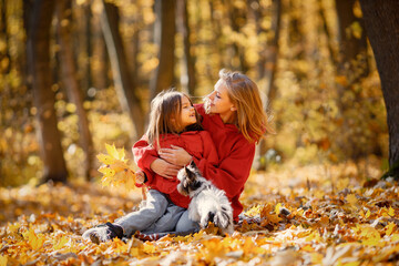 Mother and daughter sitting on a blanket in autumn forest with dog