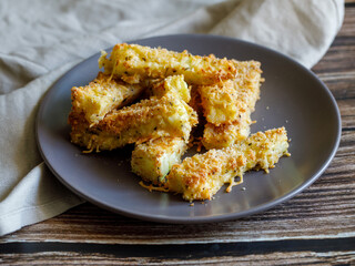 crunchy zucchini sticks breaded with breadcrumbs, parmesan cheese, spices on a black plate with grey napkin on a dark brown wooden table, side view close up