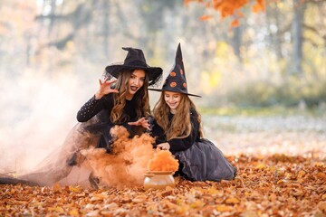 Portrait of mother and daughter in witch costumes in autumn forest