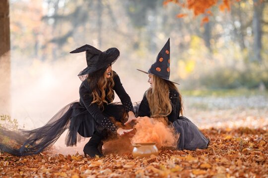 Portrait of mother and daughter in witch costumes in autumn forest