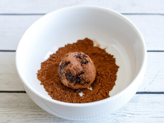 Healthy organic homemade delicious energy ball: chocolate balls cakes made from raisin, prune, dates, walnut, figs on white background, covering in bowl with cocoa carob powder. Close up top view
